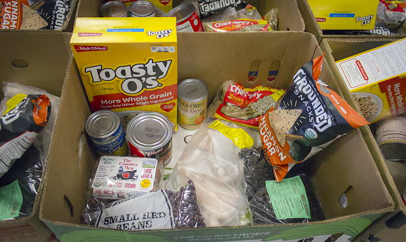 A box filled with various food items, including cereal, cans, snacks, and beans.