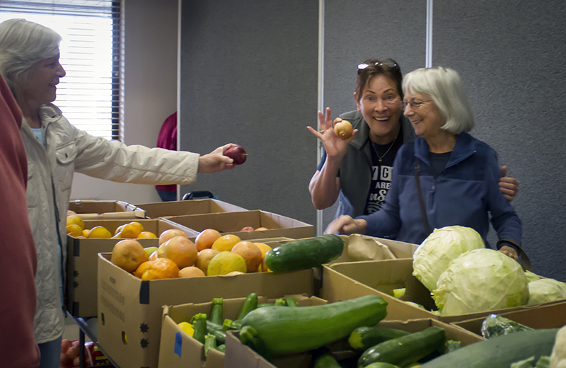 People helping people at a food distribution point, smiling and sharing produce.