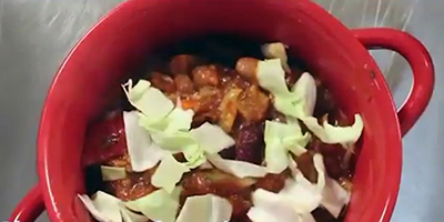 A bowl of chili topped with sliced cabbage-like garnish.