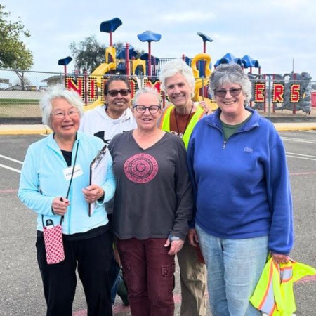 A group of five people standing in a parking area near a playground with the word "NIPOMO ELEMENTARY" visible in the background.