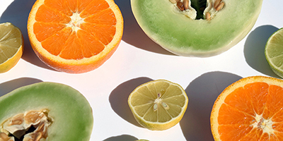 Rodajas de naranja, limón, melón y lima sobre un fondo blanco.