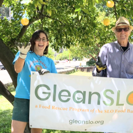Two people under a tree hold a banner for GleanSLO, a food rescue program.
