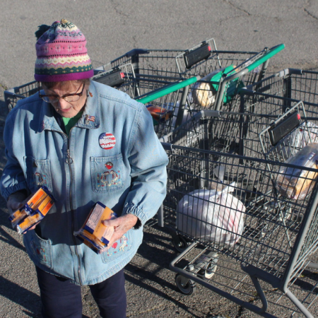 A woman holds cheese ready for distribution in front of some shopping carts.
