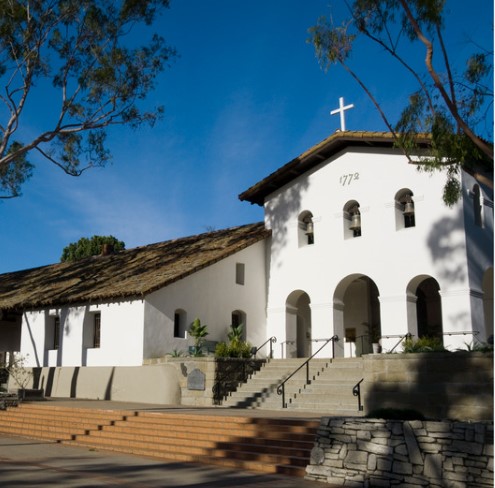 Una iglesia histórica de estilo misionero con una fachada blanca, una cruz en lo alto y el año "1772" sobre la entrada.