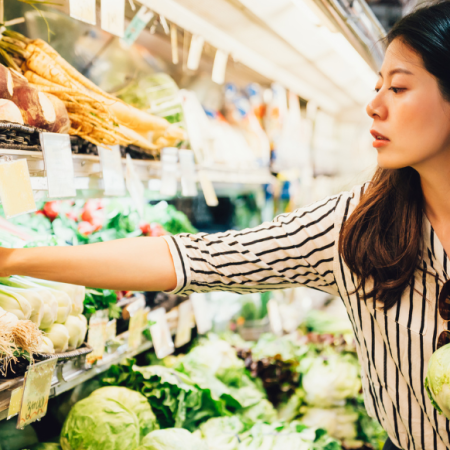 A woman grocery shopping, selecting fresh vegetables. Consider tips for saving money amid food inflation.