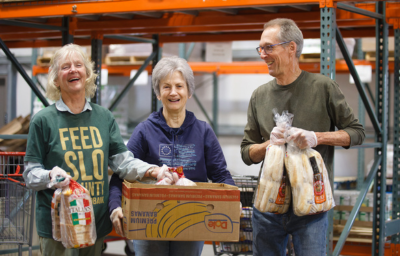 Voluntarios sonrientes organizando y transportando donaciones de alimentos en el almacén del Banco de Alimentos de SLO.