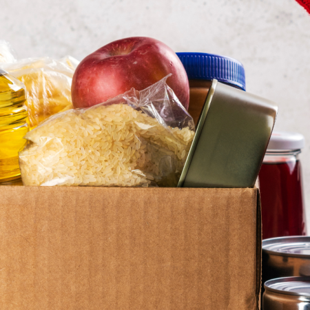 A box contains various food items like oil, rice, an apple, and canned goods, related to donating nutritious food.