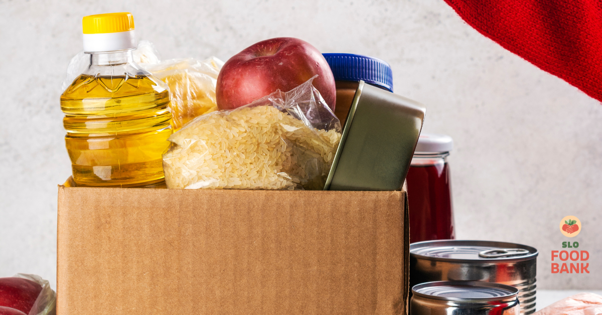 Una caja contiene diversos alimentos como aceite, arroz, una manzana y productos enlatados, relacionados con la donación de alimentos nutritivos.