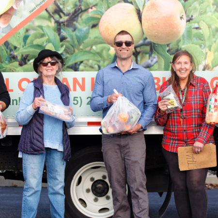 Un grupo de personas está de pie delante de un camión con alimentos en la mano, posiblemente participando en la distribución de alimentos o como voluntarios.