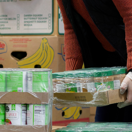 A person handling canned goods with boxes in the background, ideal for budget friendly meals.