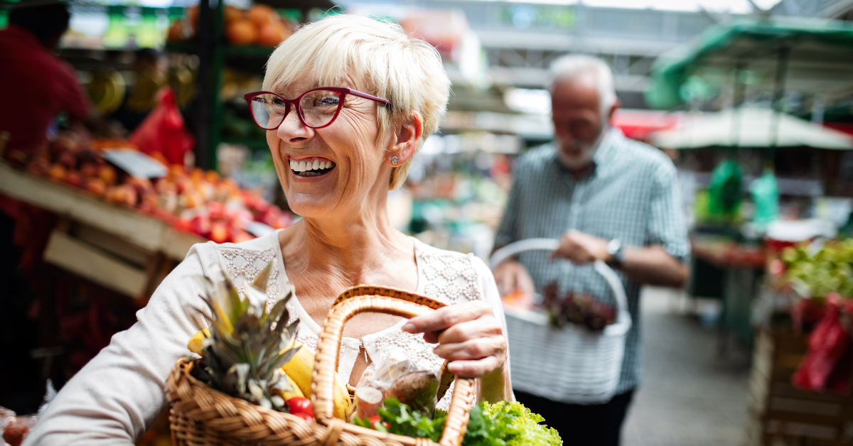 A smiling woman holding a basket of fresh produce at a market, suggesting a place where to use CalFresh EBT.
