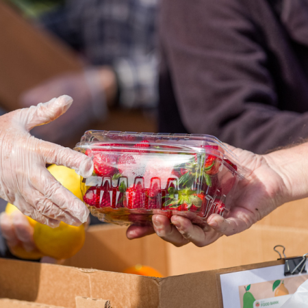 A person in gloves hands over a box of strawberries to someone, possibly at a food bank. California food benefit delay may apply.