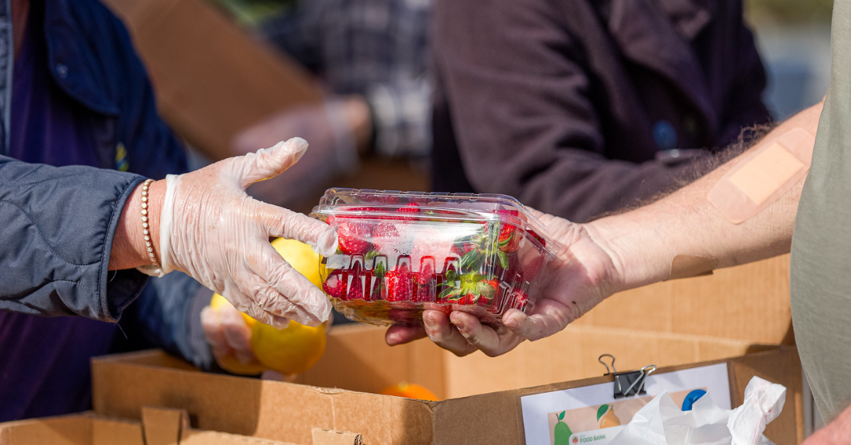 A person in gloves hands over a box of strawberries to someone, possibly at a food bank. California food benefit delay may apply.